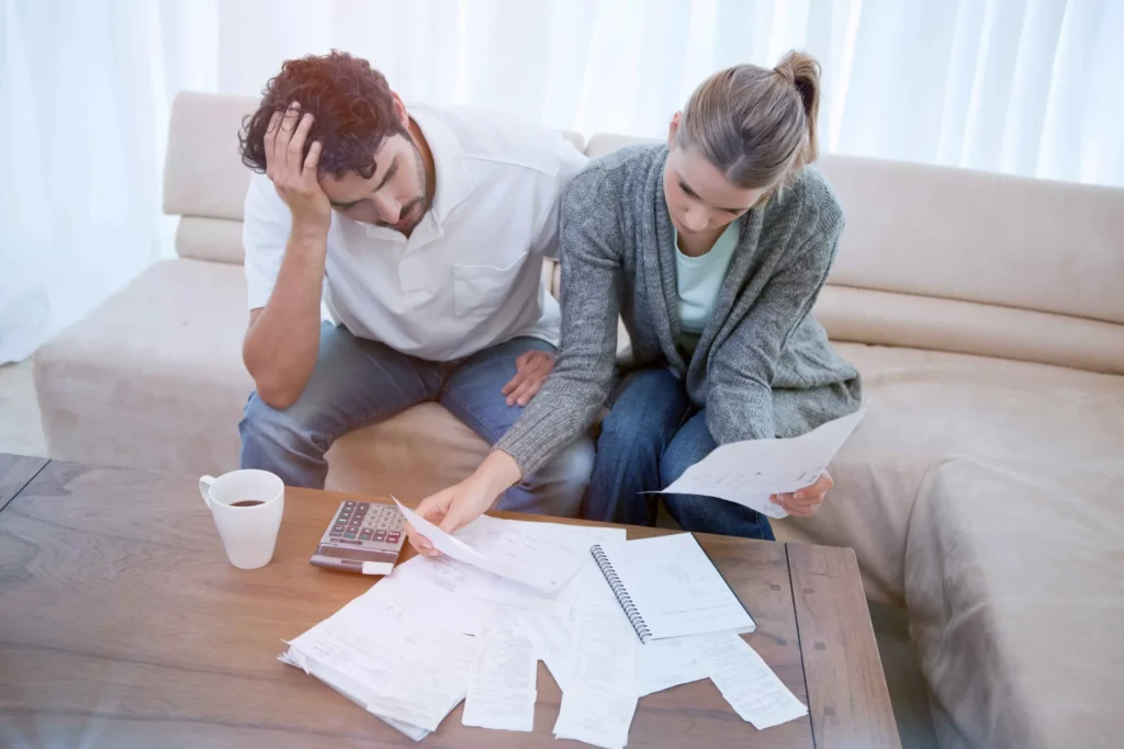 A couple looking at paperwork on their table with a calculator, both looking stressed.