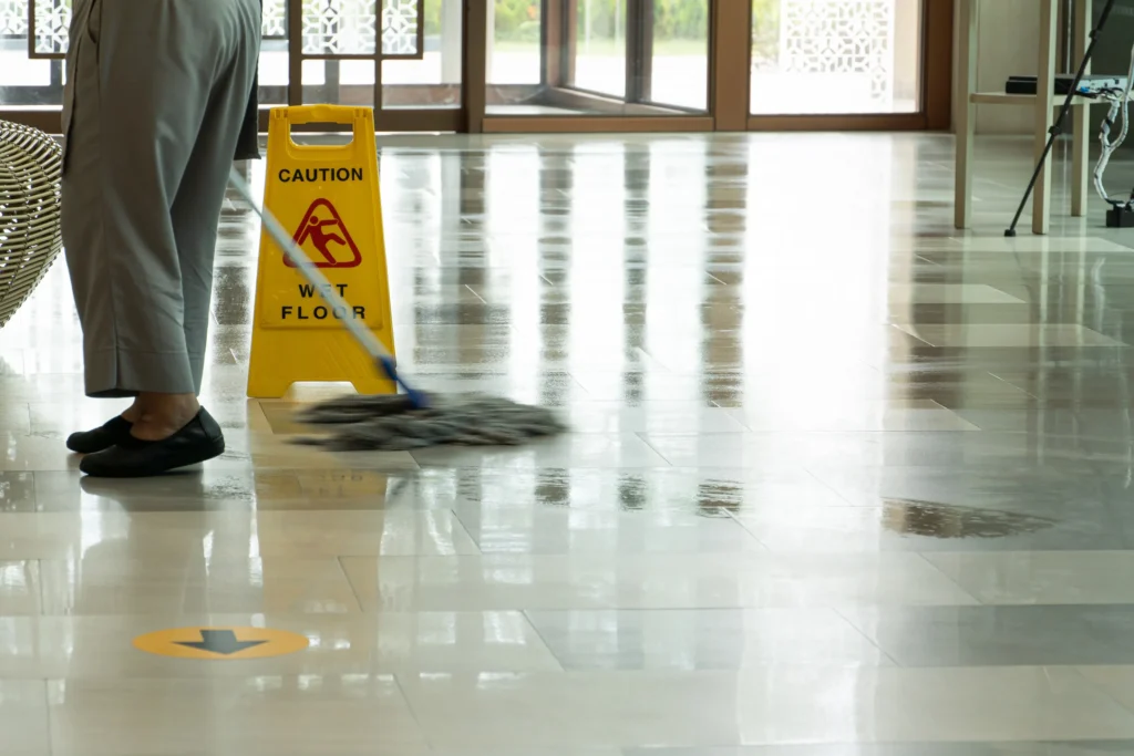 A woman mopping a lobby with a wet floor sign.