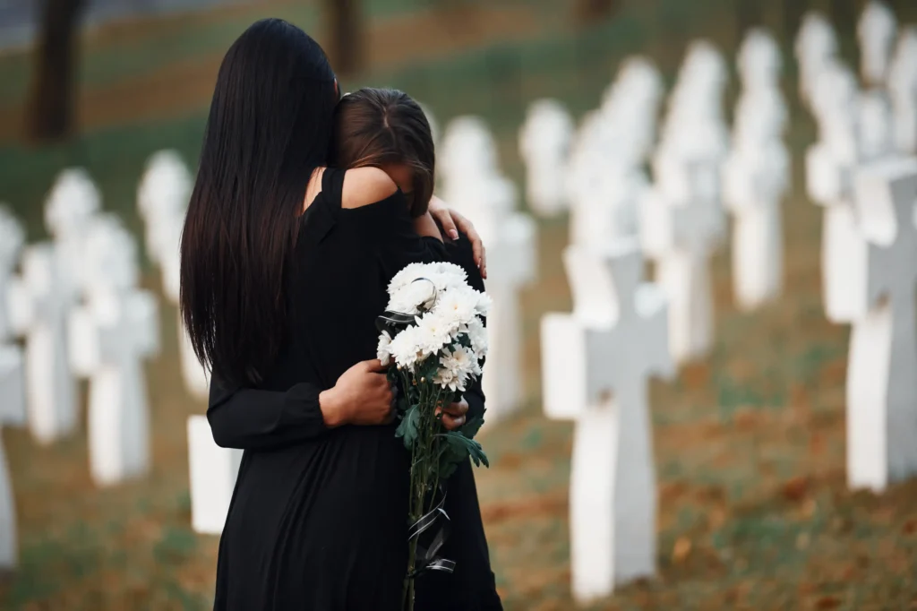Two women in black hugging in a cementary.