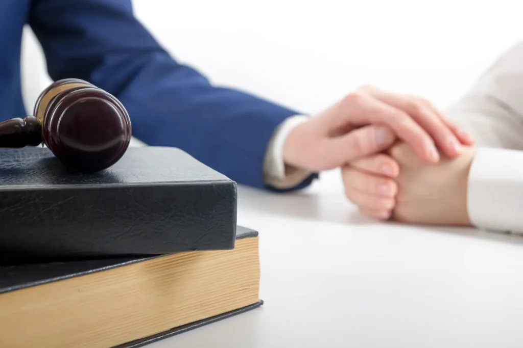 An attorney with his hand over his client's hand with a gavel and books on his desk.