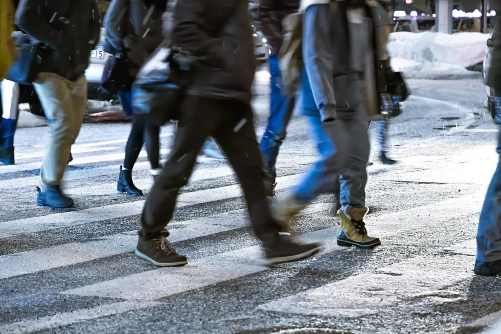 Group of pedestrians walking across a crosswalk on a wet city street, representing cases handled by an Arizona pedestrian accident lawyer.