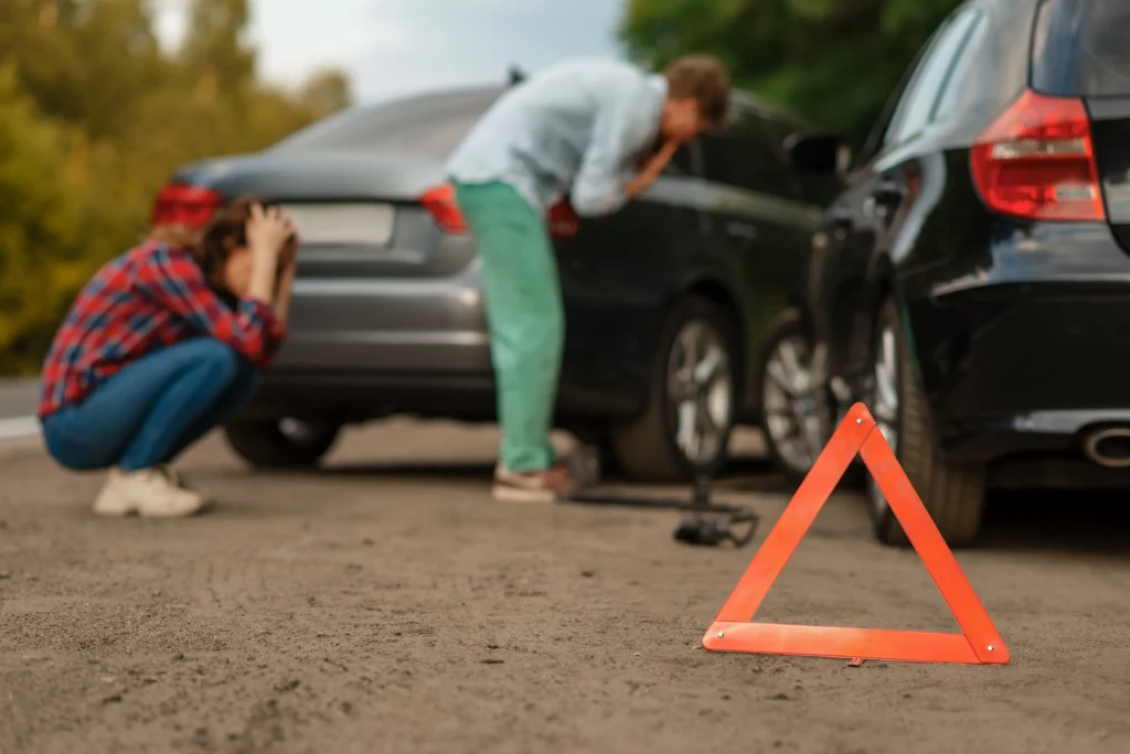 Two distressed individuals react to a car accident, with a warning triangle placed on the road, symbolizing the aftermath and legal concerns of auto collisions in Arizona.