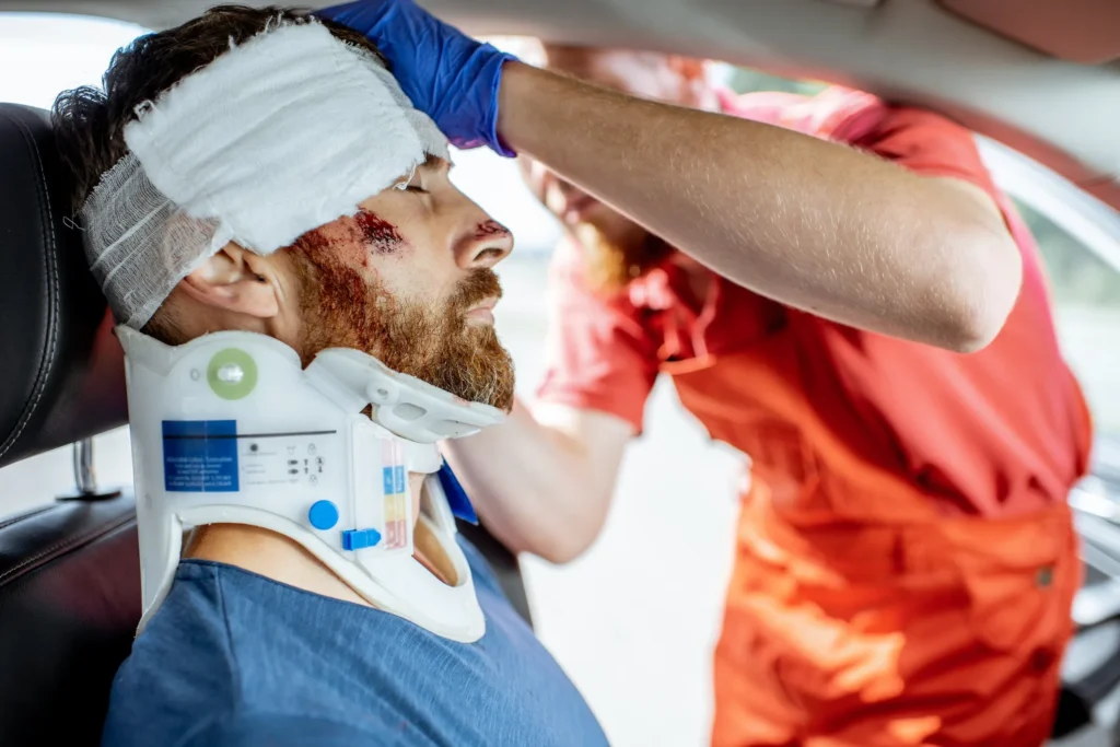 Emergency responder assisting an injured man with a head wound and neck brace after an accident, representing cases handled by an Arizona TBI attorney.
